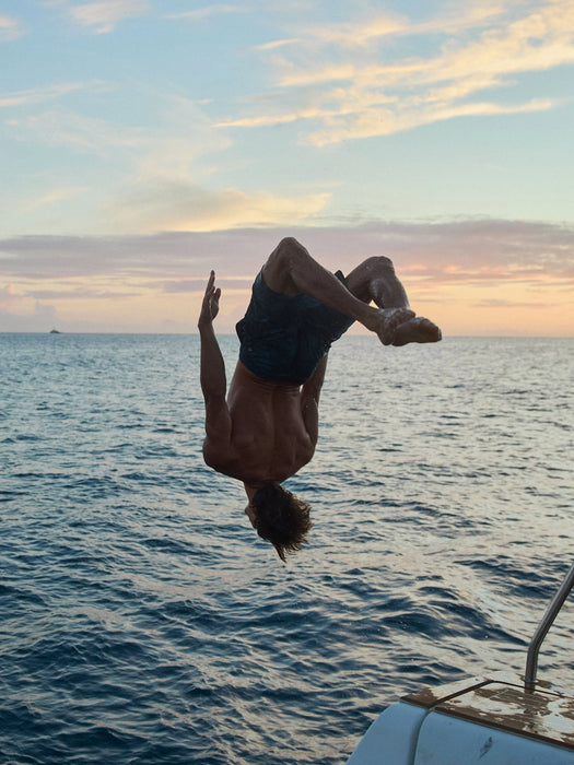 Person doing a backflip into the water at sunset