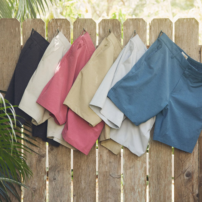 Reyn Spooner Aloha 'Aina 4 Way Stretch Shorts in Black, Grey, Nantucket Red, Khaki, Stone and Medium Blue hanging on a wood fence.
