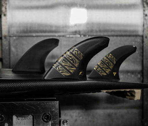 Futures Alpha Vector 3/2 size Large thruster fin set made of black recycled carbon with gold accents  installed in a surfboard