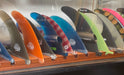 Many sizes of surfboard fins being displayed on a solid heavy wood base