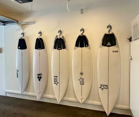 Five surfboards shown on a wall hang ups hangers are show in use.