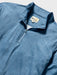 Close-up of a blue quarter-zip pullover with a subtle white line Tapa pattern of waves surfboards and and other Hawaiian elements; Reyn Spooner label inside the collar.