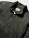 Close-up of a dark charcoal gray quarter-zip pullover with a subtle white line Tapa pattern of waves surfboards and and other Hawaiian elements; Reyn Spooner label inside the collar.