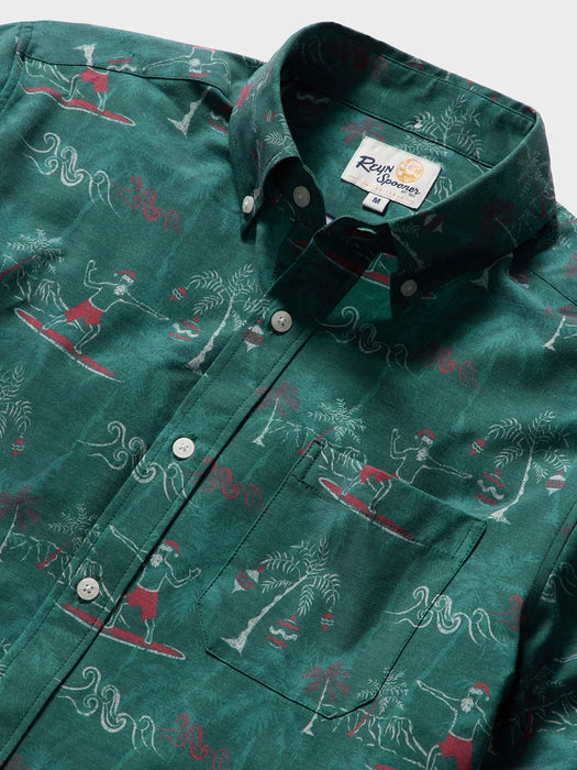 Close up of Surfin' Santa Performance Button Front Collared Short Sleeve Pine colored Aloha Shirt depicts Santa Surfing Waikiki with Diamondhead in the background.