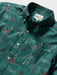 Close up of Surfin' Santa Performance Button Front Collared Short Sleeve Pine colored Aloha Shirt depicts Santa Surfing Waikiki with Diamondhead in the background.