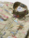 Close up of a button-up collared classic shirt with an all-over khaki fabric map print featuring Route 66 motifs, illustrated landmarks, and small colorful details.