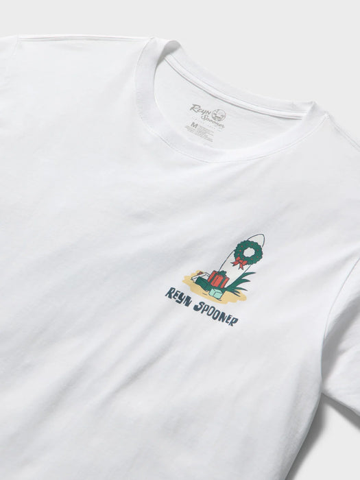 A close-up of a navy blue t-shirt front view featuring a small graphic on the left chest of a surfboard decorated with a green Christmas wreath and presents, with the text 'REYN SPOONER' printed below.