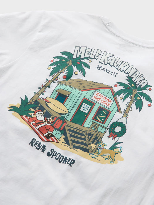 Close-up of a white t-shirt featuring a graphic of a festive Hawaiian beach scene with Santa Claus, a surf hut, palm trees, and the text 'MELE KALIKIMAKA HAWAII' and 'REYN SPOONER'.