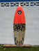 A shortboard surfboard bottom view with a bright orange and a grey/black camouflage patterned with 5 Futures fin boxes, displayed against a 6' white stucco wall.