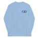 Light blue long-sleeve crewneck shirt shown from the front, featuring a blue and grey graphic print of surfboards, palms and hut with the text 'KIMO'S SURF HUT' inside a double oval on the left chest.