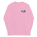 Light pink long-sleeve crewneck shirt shown from the front, featuring a blue and grey graphic print of surfboards, palms and hut with the text 'KIMO'S SURF HUT' inside a double oval on the left chest.