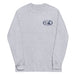 Grey long-sleeve crewneck shirt shown from the front, featuring a blue and grey graphic print of surfboards, palms and hut with the text 'KIMO'S SURF HUT' inside a double oval on the left chest.